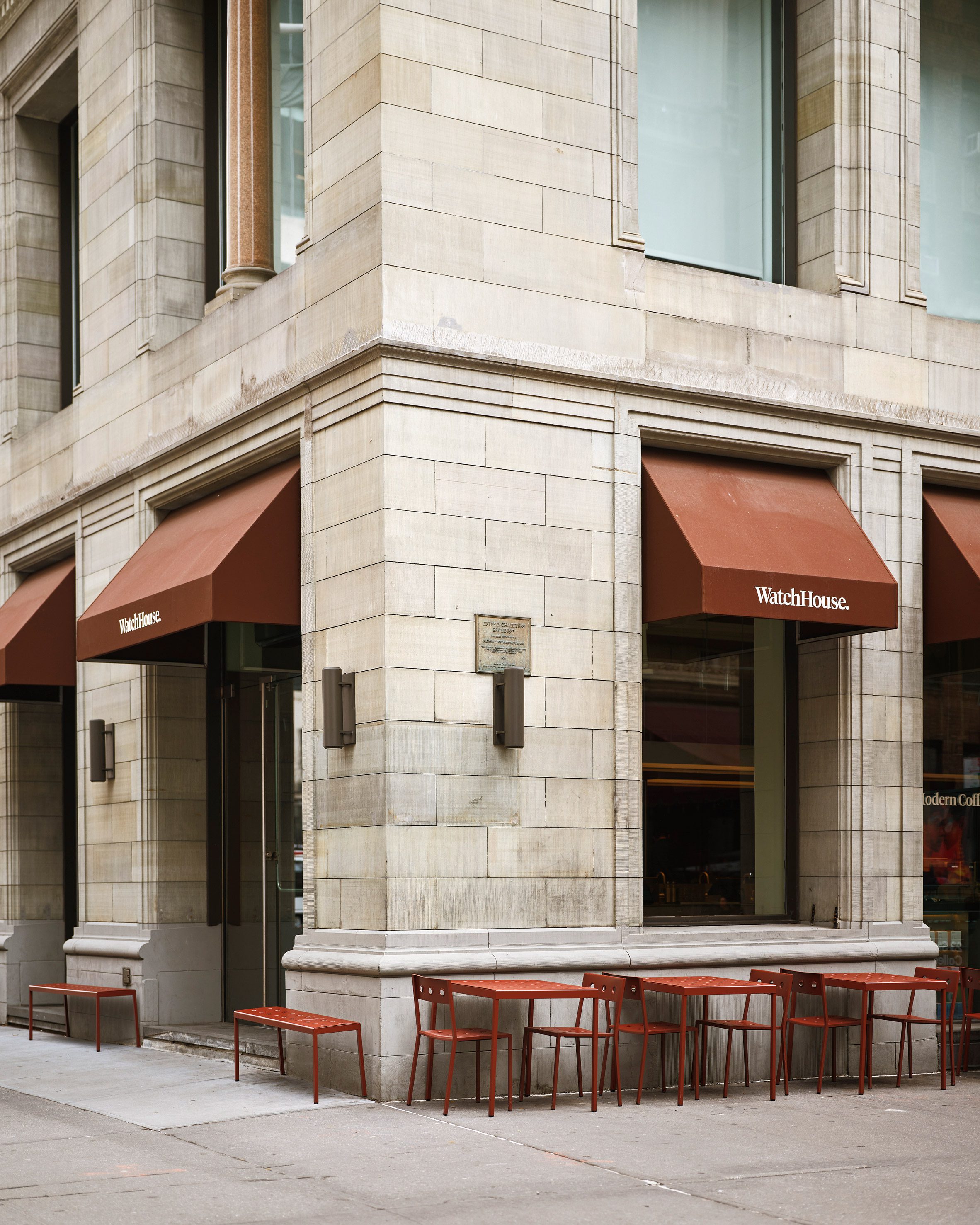 Historic stone building with russet-hued window awnings and furniture outside