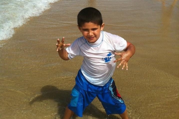 A boy at the beach posing in the shallow water.