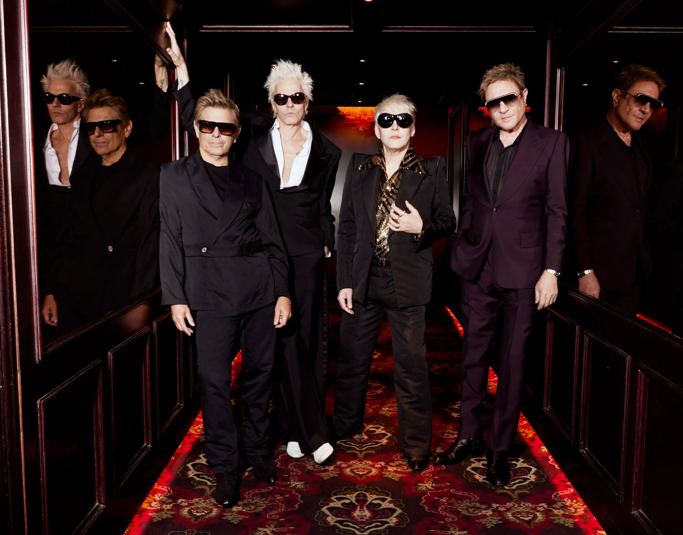 Duran Duran band members Roger Taylor, John Taylor, Nick Rhodes, and Simon Le Bon posing in suits and sunglasses.