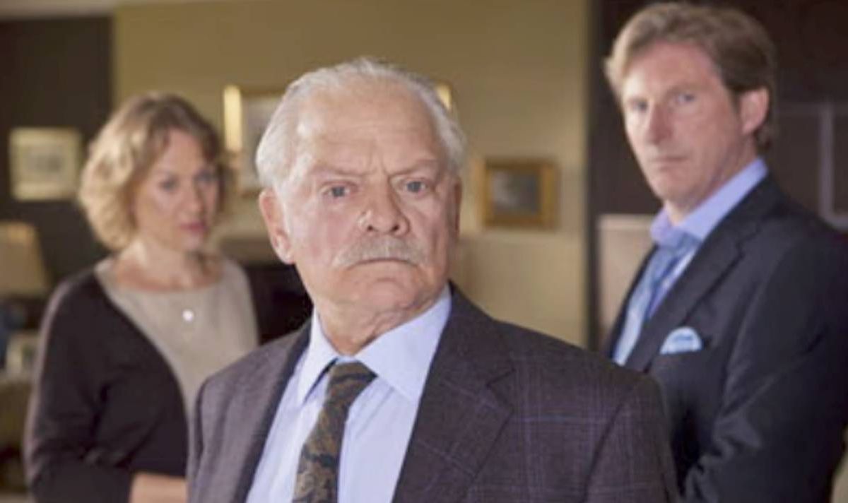 A man in a suit look serious as a man and a woman stand behind him