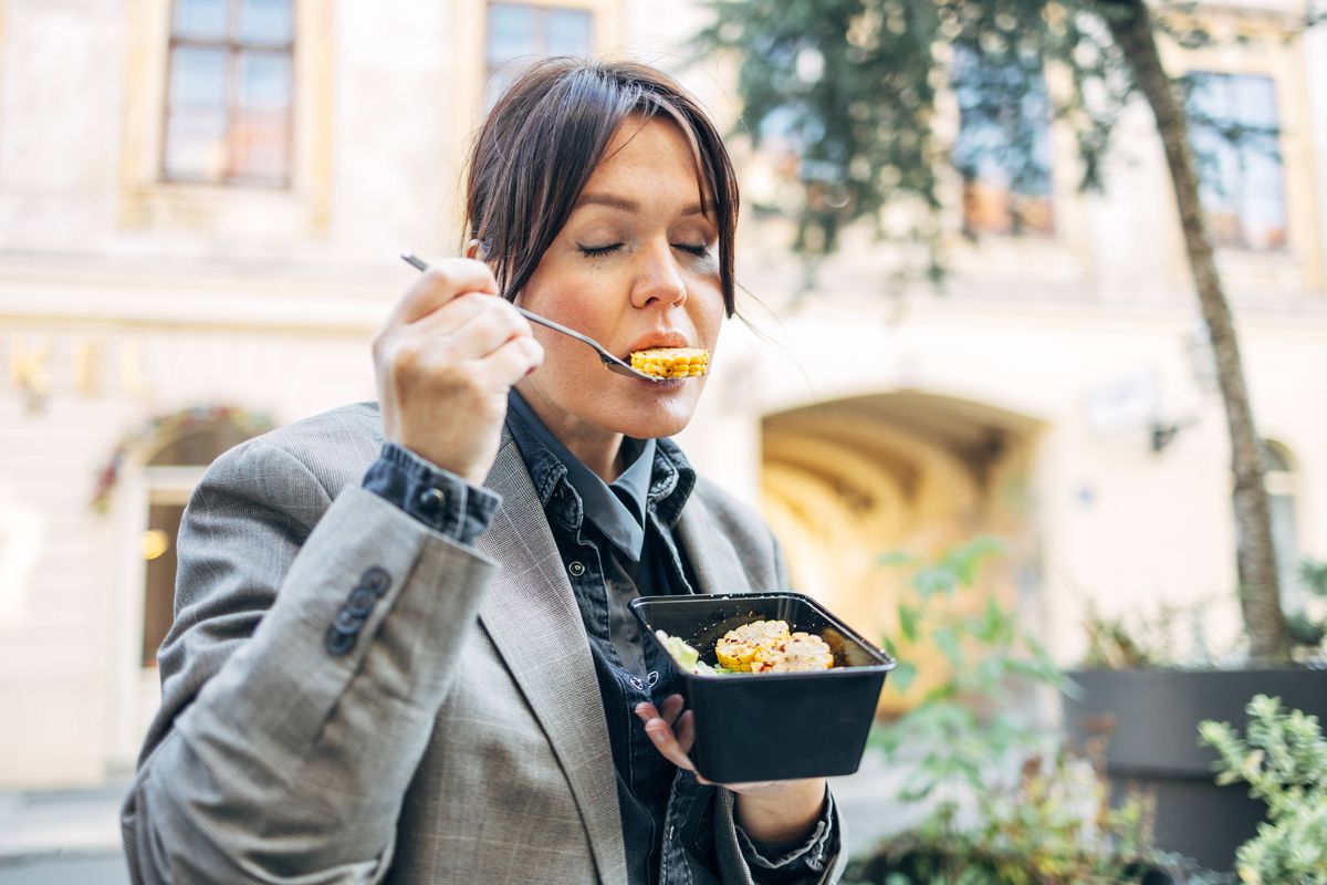 Woman closing eyes enjoying meal from a takeout box outdoors