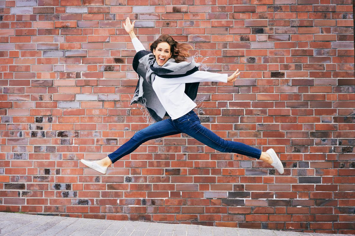 Happy young woman jumping in the air in front of brick wall