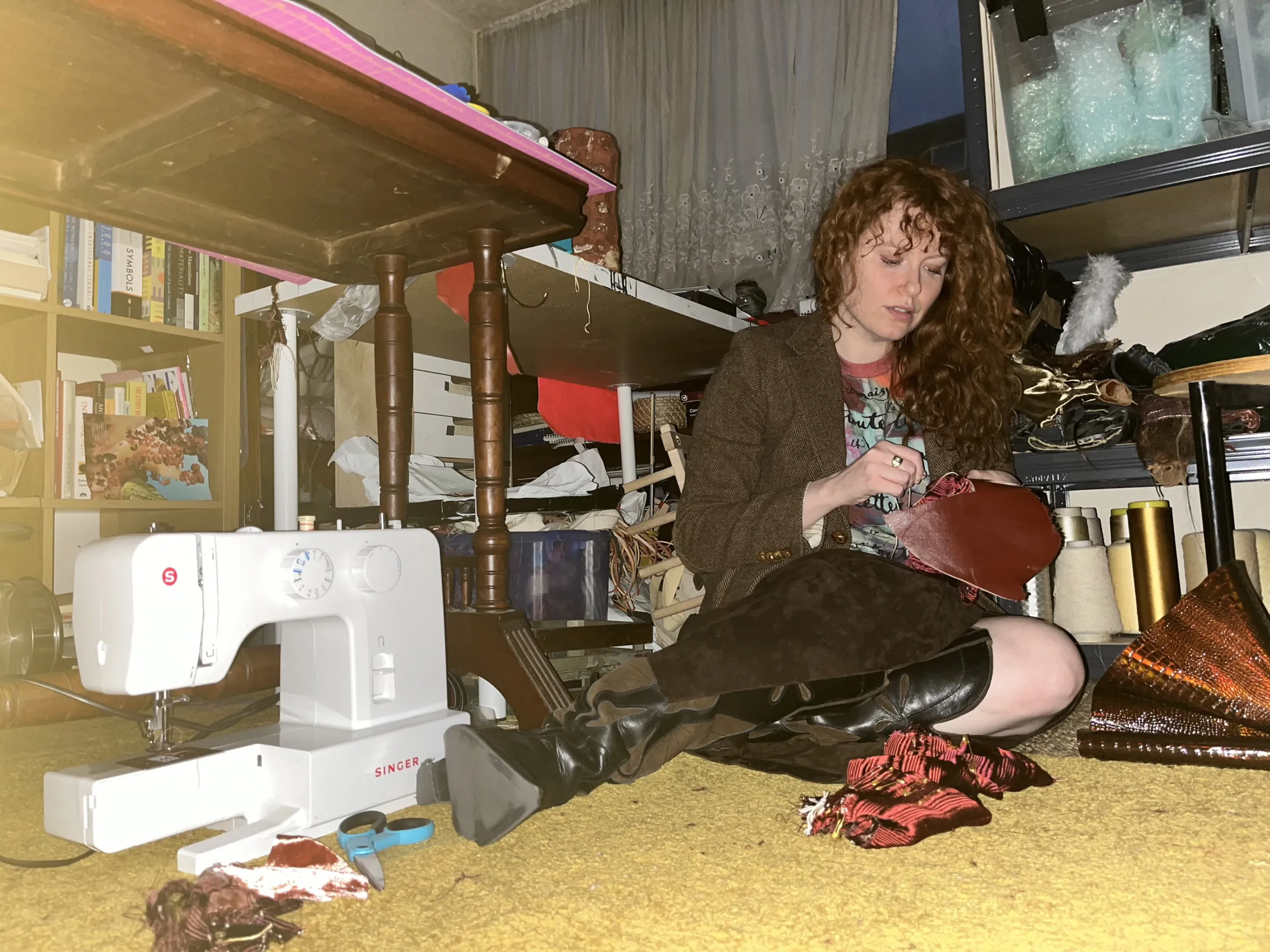 Artist Kathryn MacCorgarry Gray sewing a red fabric piece while sitting on the floor.