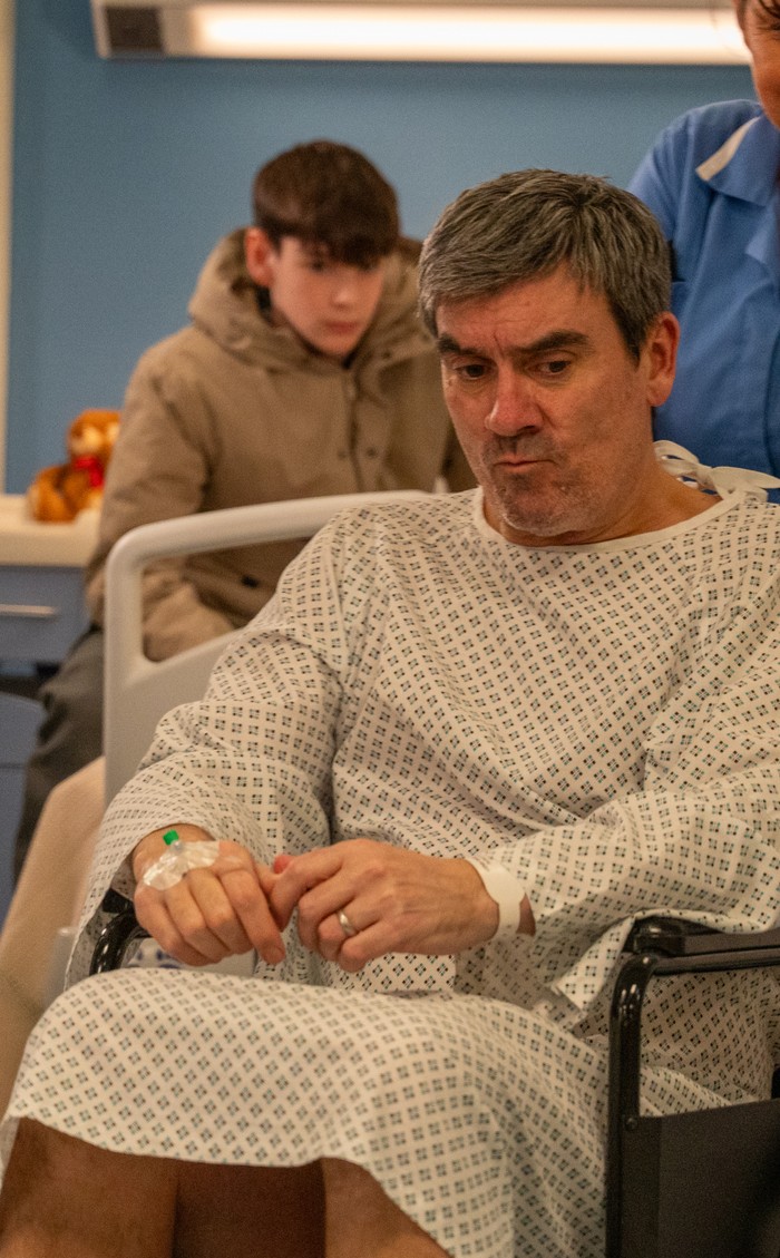 11_05_emm_kyle_cain_01 Kyle watches Cain being pushed through a hospital corridor in his wheelchair in a scene from Emmerdale