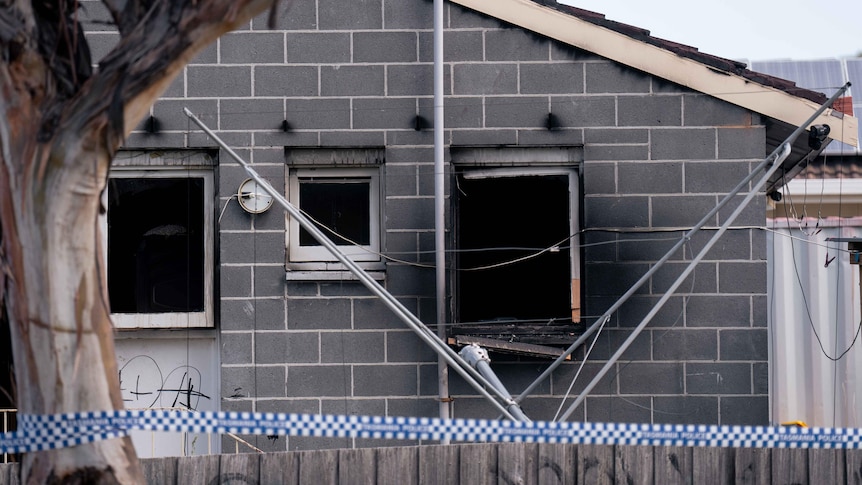 A burnt-out house with police tape strung across a fence.