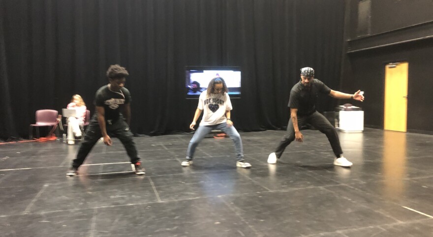 Three performers rehearse in a black-box theater
