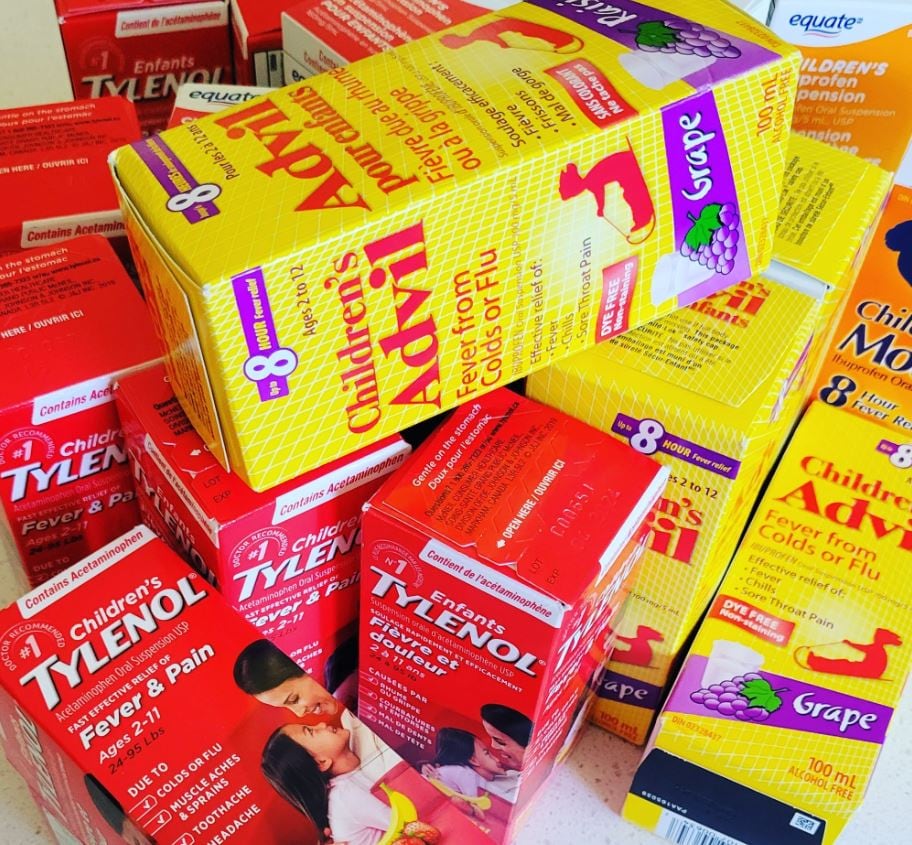 A pile of red and yellow boxes of children's Tylenol and Advil medicine on a kitchen counter.