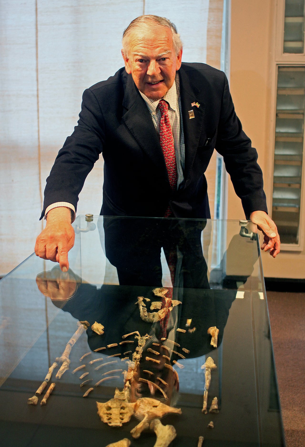 A man stands beside a table with the fossils of an early humanoid laid out on the table.