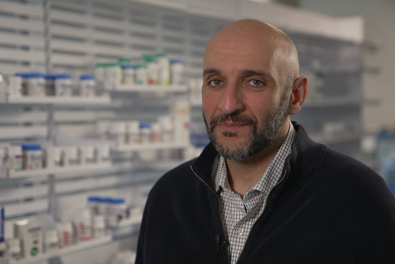A man stands with shelves of medications behind him.