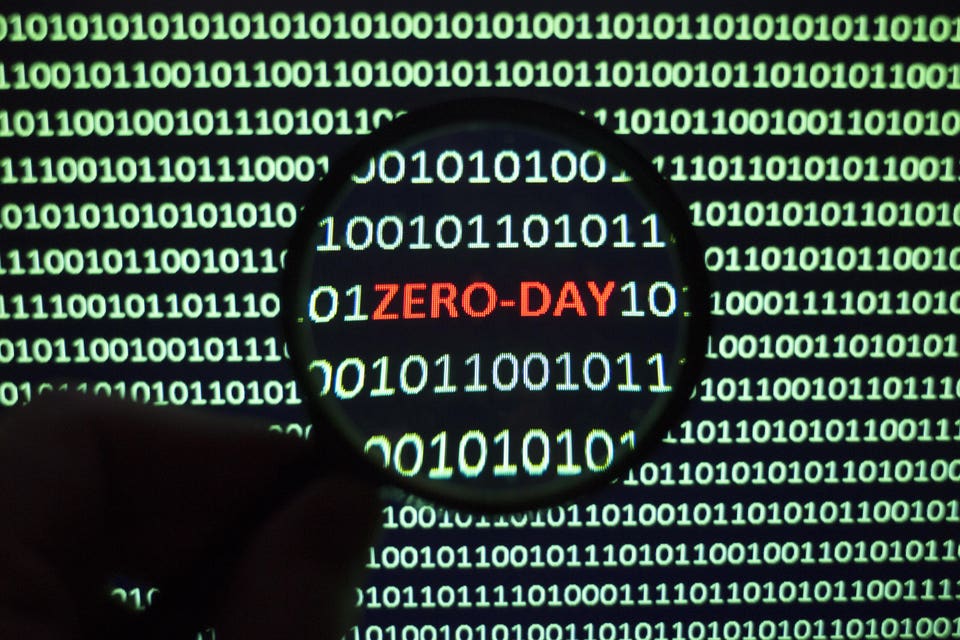 Zero-Day in red under a magnifying glass amongst green binary code.