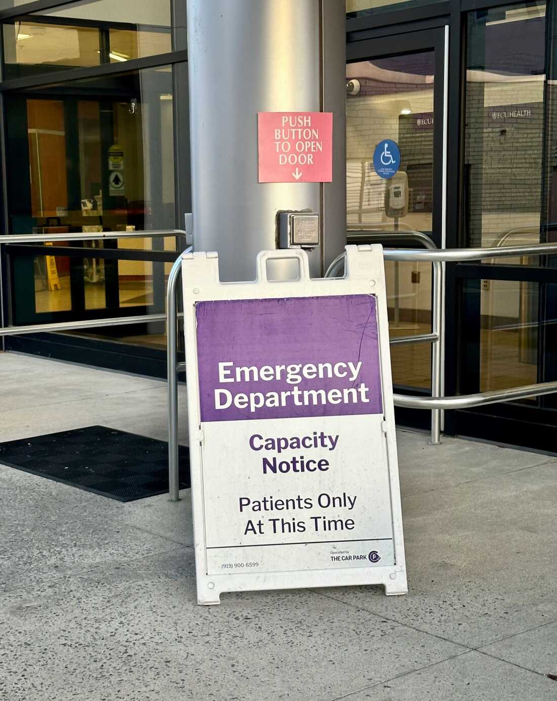 A “Capacity Notice” sandwich-board-style sign outside the ECU Health Medical Center emergency room in Greenville, North Carolina. It warns that anyone who is not a patient must wait outside.