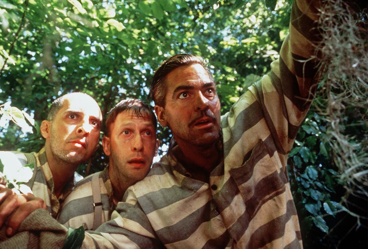 Three men in black and white striped prison jumpsuits stand in wooded area.