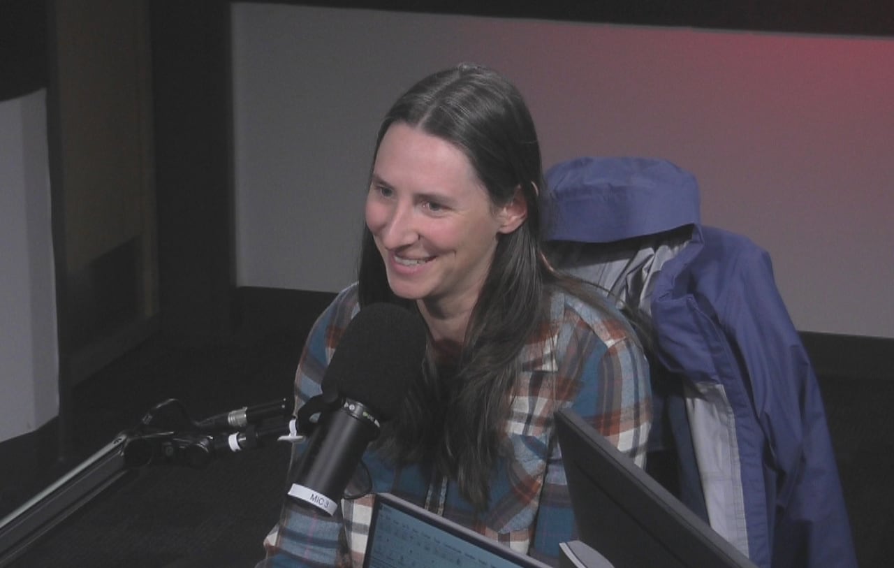 A woman in a plaid shirt sits in a radio studio behind a microphone