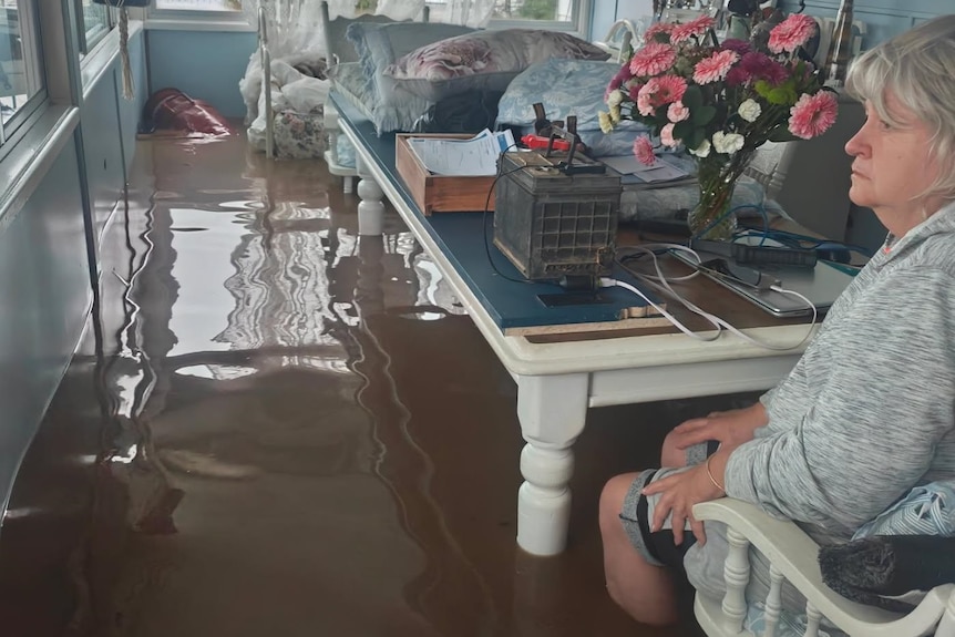 Debra Emerton sits at a table in her flooded home.
