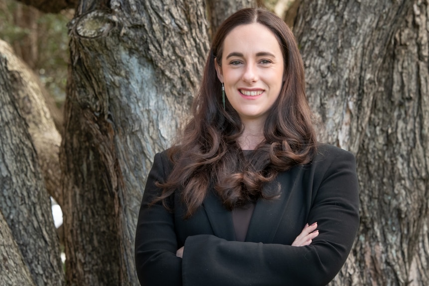 Lara Greaves with her arms crossed standing in front of a tree.