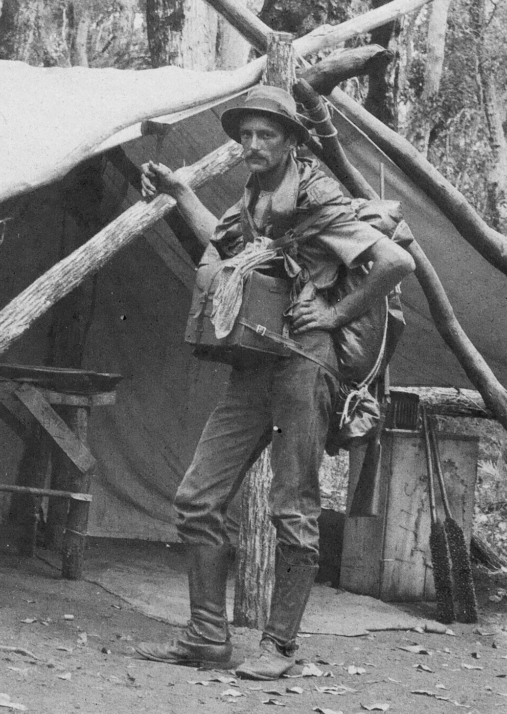 Black and white photo of a man near timber and canvas hut.