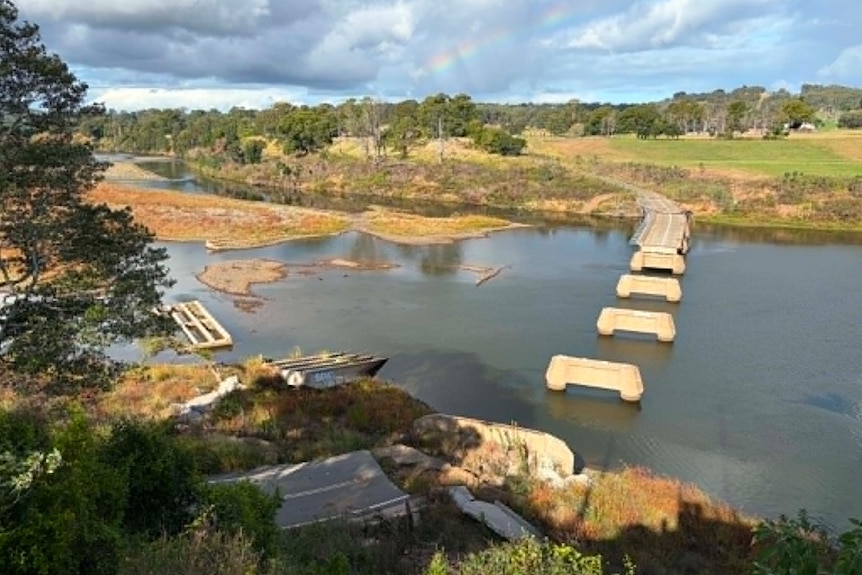 The concrete footings of a former bridge stand above the river in a line to the road.