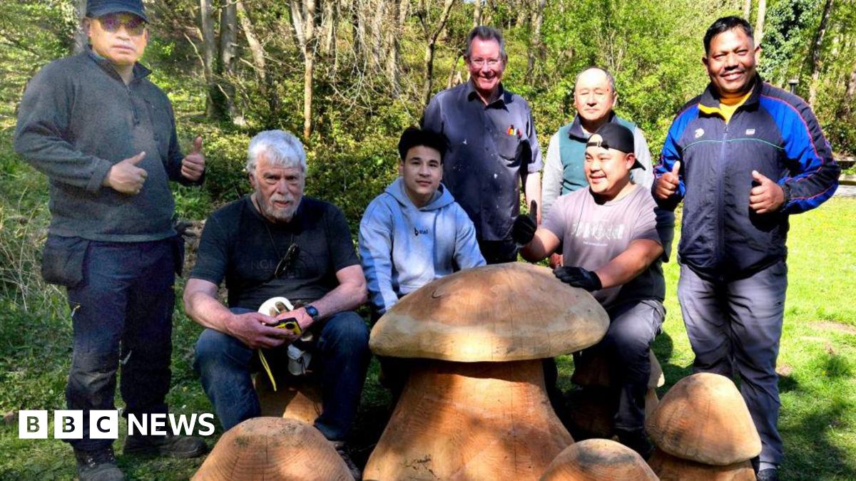 A group of men stand in a woodland area alongside large wooden toadstools.