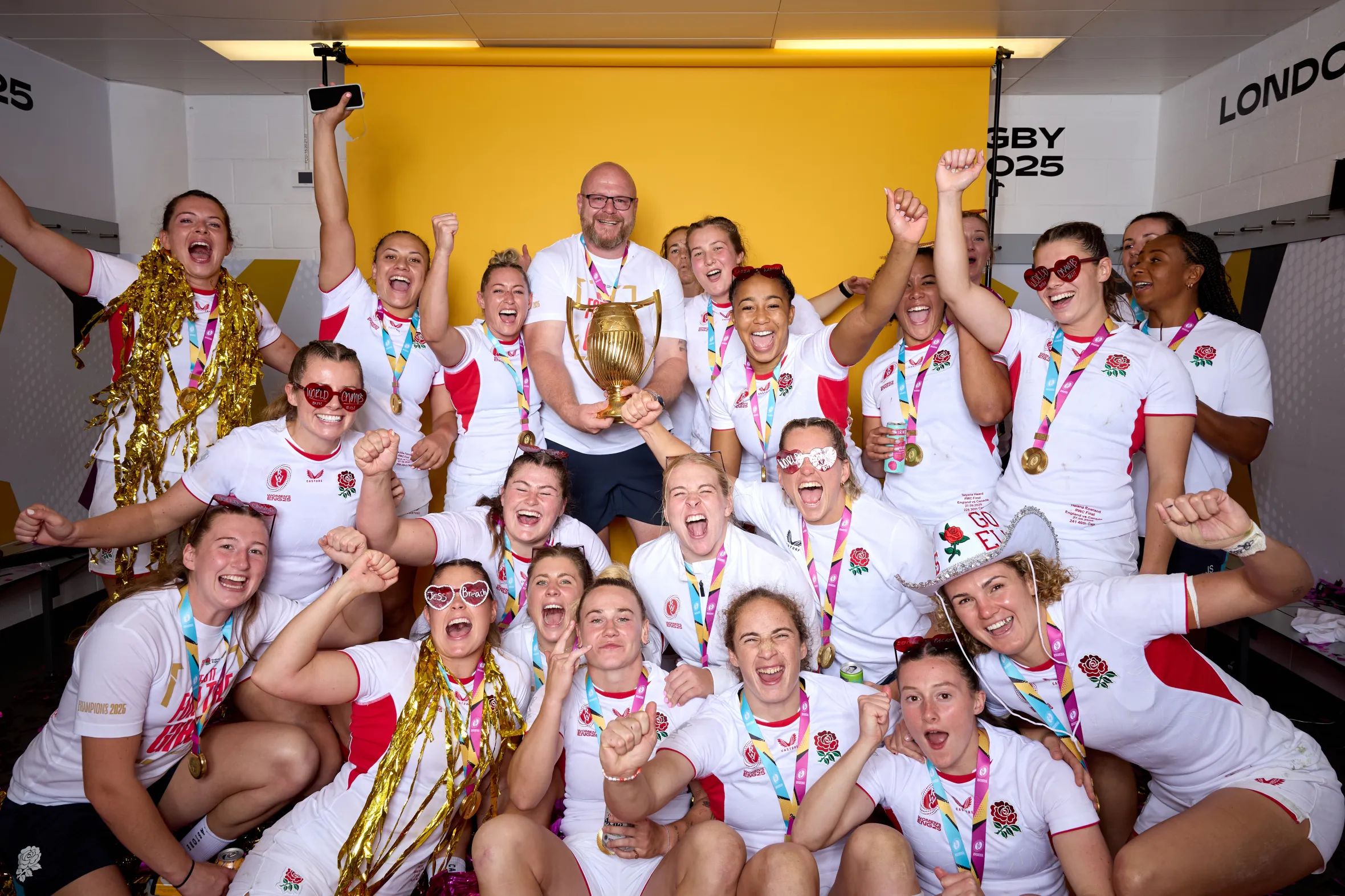 The victorious England women's rugby team and staff celebrate with the Rugby World Cup 2025 trophy.
