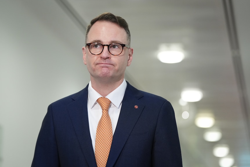 A serious-looking man in a suit and glasses.