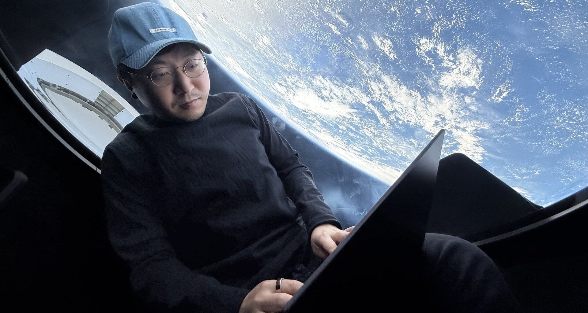 Mission commander Chun Wang works on his laptop with Earth looming outside the window of SpaceX's Dragon capsule during the Fram2 mission in 2025. (Chun Wang / SpaceX via X)