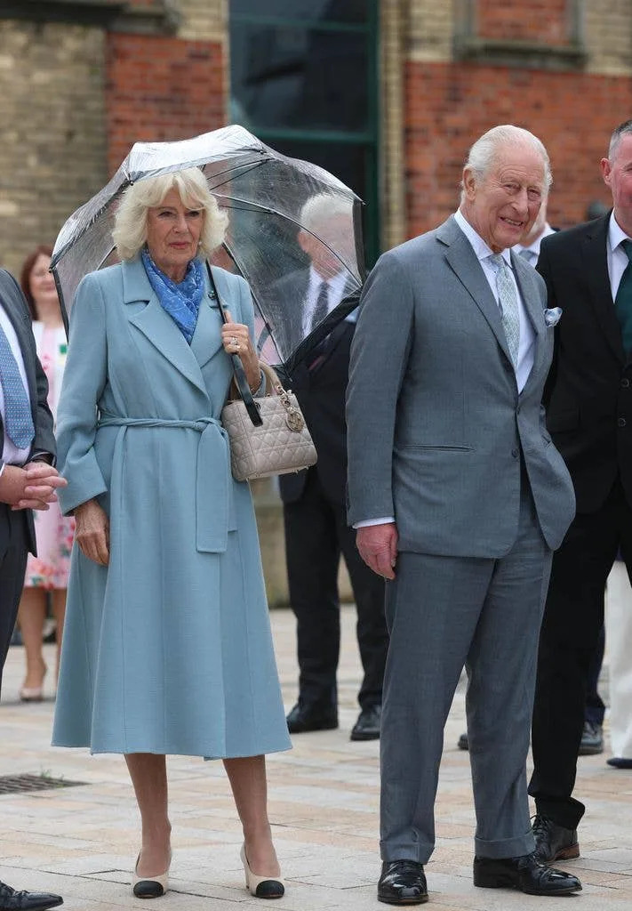 King Charles and Queen Camilla holding umbrella outside