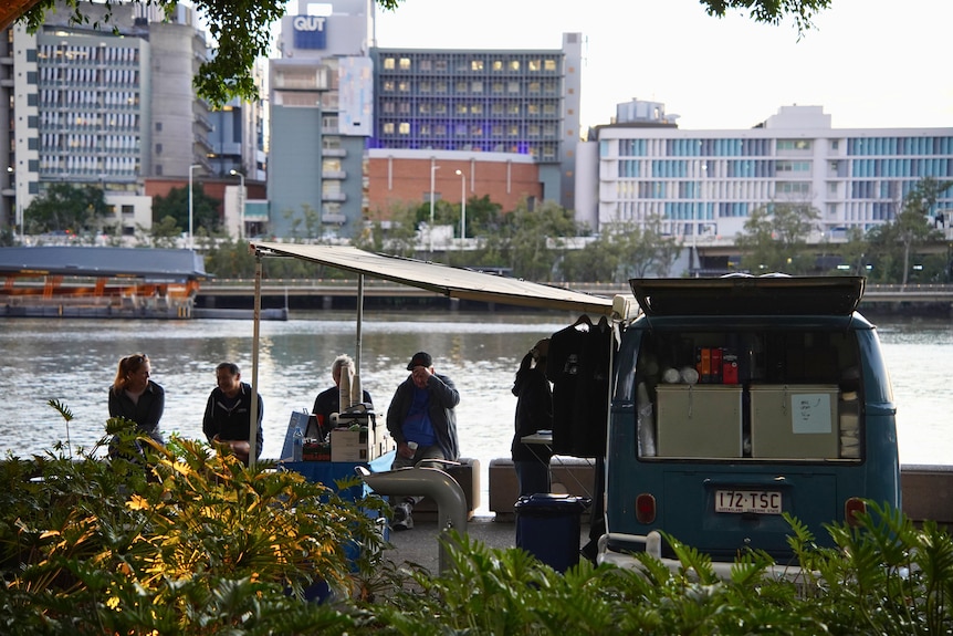People sitting on a ball beside the river with a coffee van parked next to them.