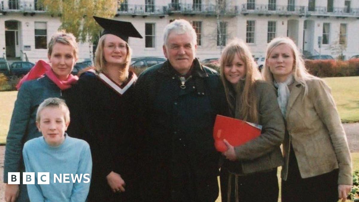 An old photo of a family standing together. Michael Gwilliam is in the middle of his four daughters, with one of them wearing a graduation cap and gown. A young boy crouches down in front of them.