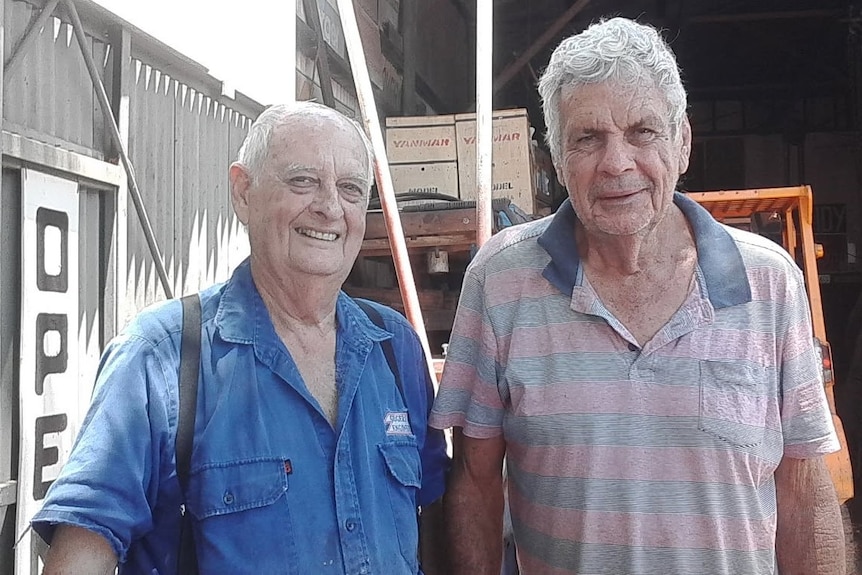 Two men in a shed smile at the camera