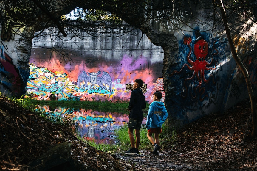 Two children stand in an archway, looking at walls covered with colourful graffiti and artworks.