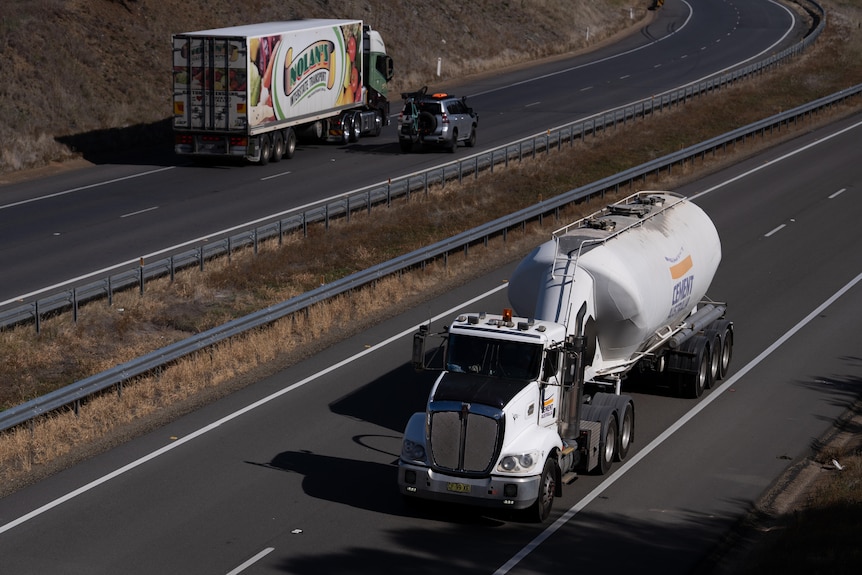 Two trucks drive in opposite directions on a highway.
