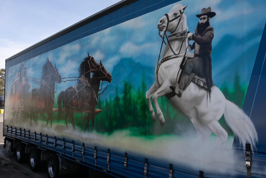 A close up of a mural-inspired illustration of horses running through nature on the side of a blue truck.