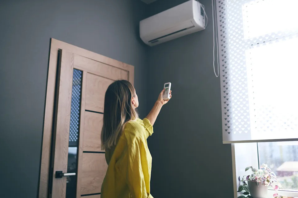 Woman using remote control to turn on air conditioning unit, staying cool at home