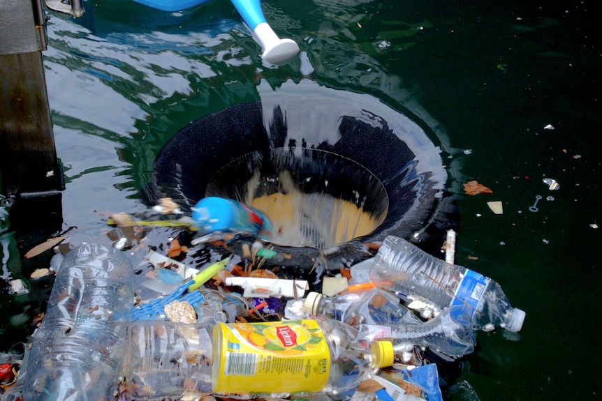 A circular void in flat water with a range of plastic bottles and other floating rubbish about to be sucked in.