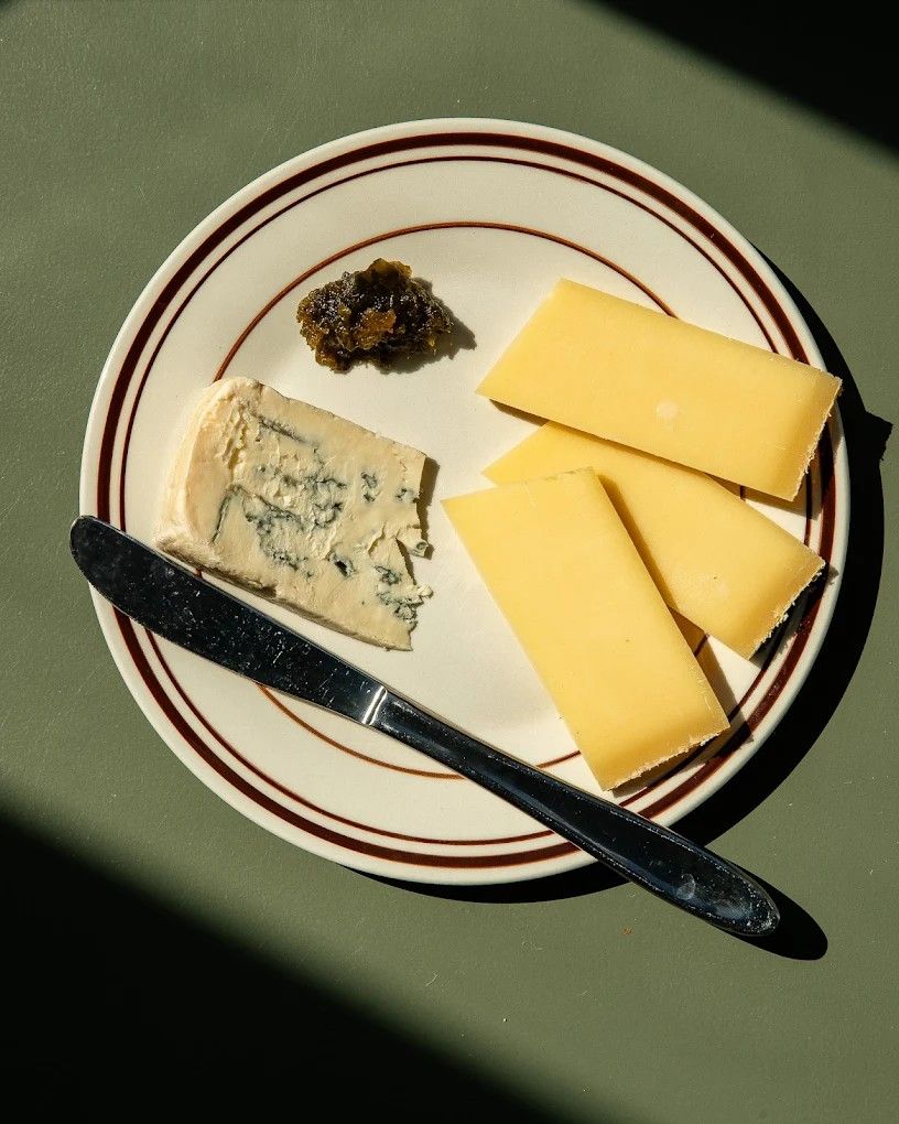 A plate filled with cheese and pickled paste, placed atop a green surface in the sun.