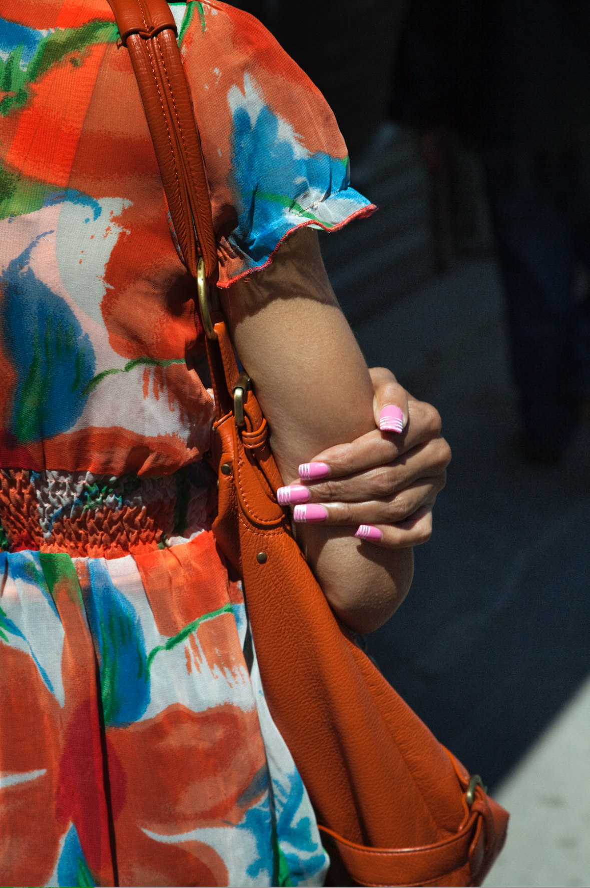 A person in a colorful dress holding an orange handbag, with pink and white striped nails.