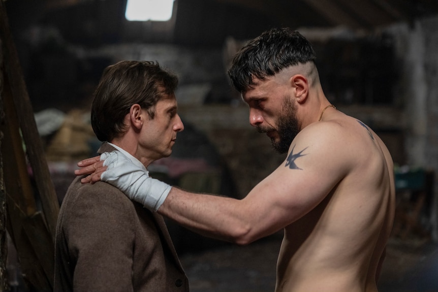 A TV still of Richard Gadd, 37, shirtless, hand on the shoulder of Jamie Bell, 40, in a brown suit, both looking serious.