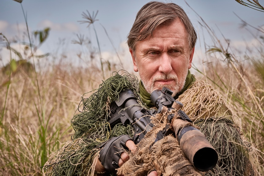 A man in camoflauge holds a rifle.