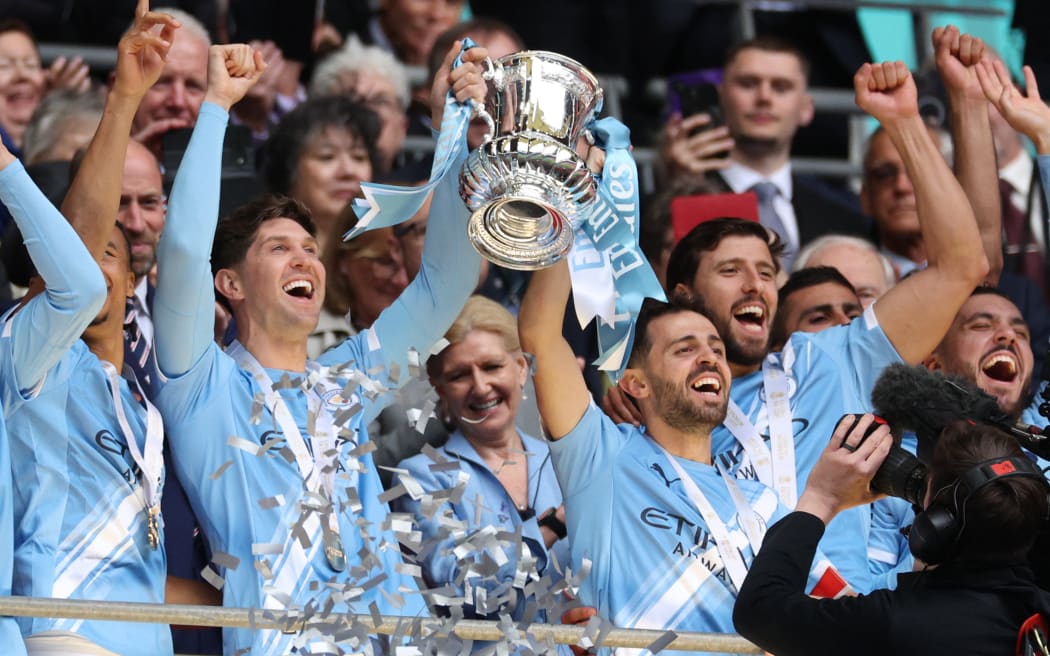 Manchester City's English defender #05 John Stones (L) and Manchester City's Portuguese midfielder #20 Bernardo Silva (R) lift the trophy as City players celebrate after the English FA Cup final football match between Chelsea and Manchester City at Wembley stadium in London, on May 16, 2026. Manchester City won the game 1-0. The third FA Cup success of Guardiola's reign ended City's run of two successive defeats in the final. (Photo by Adrian Dennis / AFP) / NOT FOR MARKETING OR ADVERTISING USE / RESTRICTED TO EDITORIAL USE