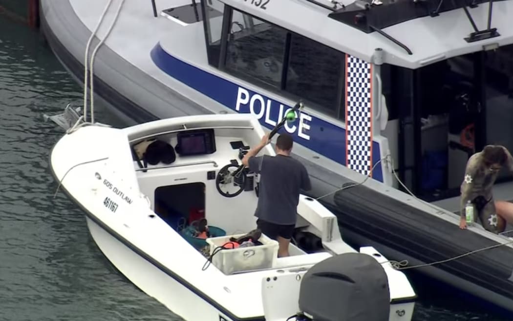 Vision shows a man returning a speargun to a small boat that was tethered to a Water Police vessel.