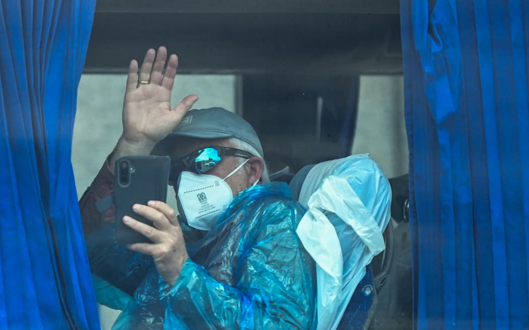 A passenger from the Dutch flagged hantavirus-stricken cruise ship MV Hondius waves aboard a military bus after being transferred by boat to the industrial port of Granadilla de Abona on the island of Tenerife in Spain's Canary Islands on May 10, 2026. Repatriation flights for the nearly 150 passengers onboard the ship hit by a deadly hantavirus outbreak began as passengers were transferred to shore on smaller vessels then by bus to the airport to be flown home after weeks at sea. (Photo by JORGE GUERRERO / AFP)