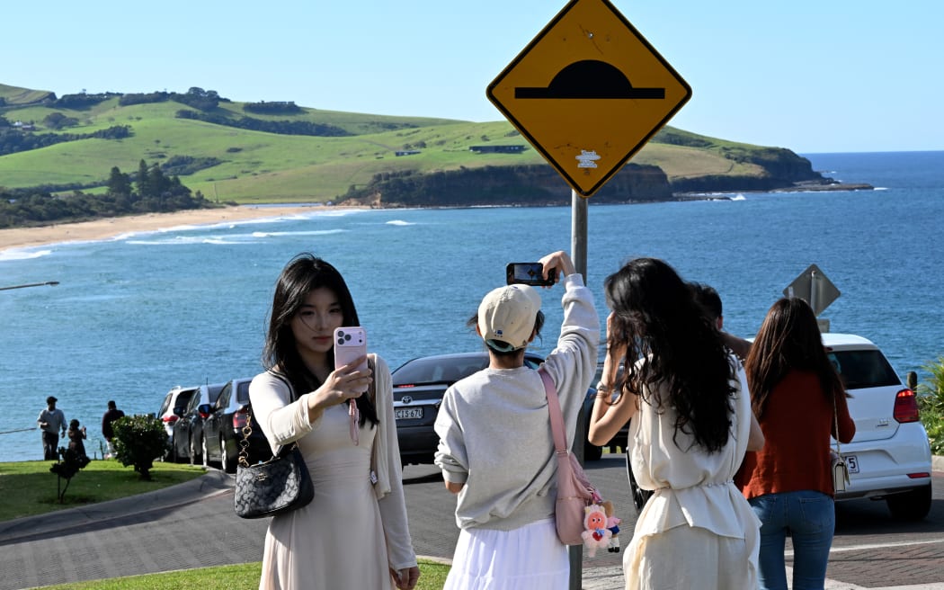 This picture taken on April 27, 2026 shows tourists taking photos on a street in Gerringong, about a two-hour drive south of Sydney. Viral posts of an Australian street dubbed the country's "most beautiful" have enticed coachloads of visitors to a picturesque seaside town -- and locals have had enough of it. (Photo by Saeed KHAN / AFP) / To go with AFP story Australia-tourism-internet by Oliver Hotham
