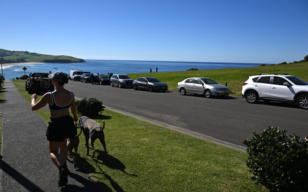 This picture taken on April 27, 2026 shows a resident walking her dogs along a street in Gerringong, about a two-hour drive south of Sydney. Viral posts of an Australian street dubbed the country's "most beautiful" have enticed coachloads of visitors to a picturesque seaside town -- and locals have had enough of it. (Photo by Saeed KHAN / AFP) / To go with AFP story Australia-tourism-internet by Oliver Hotham