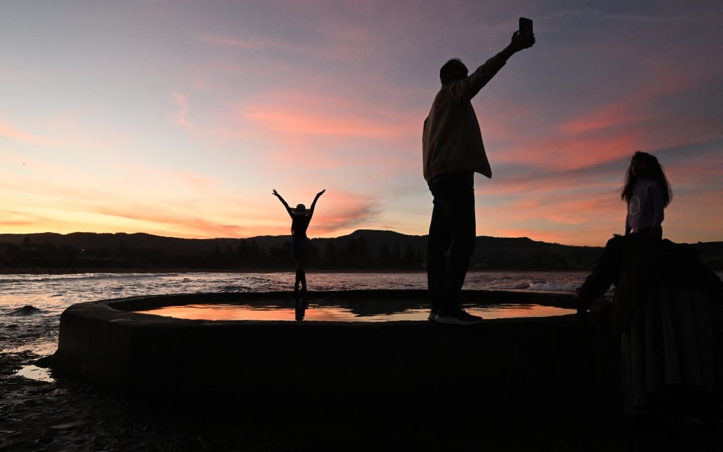 This picture taken on April 27, 2026 shows tourists photographing the sunset at the end of a well-known street in Gerringong, around a two-hour drive south of Sydney. Viral posts of an Australian street dubbed the country's "most beautiful" have enticed coachloads of visitors to a picturesque seaside town -- and locals have had enough of it. (Photo by Saeed KHAN / AFP) / To go with AFP story Australia-tourism-internet by Oliver Hotham