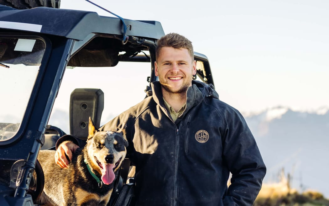 Richie Lamming is a smiling man in a thick jacket standing next to a truck with his arm around a dog.