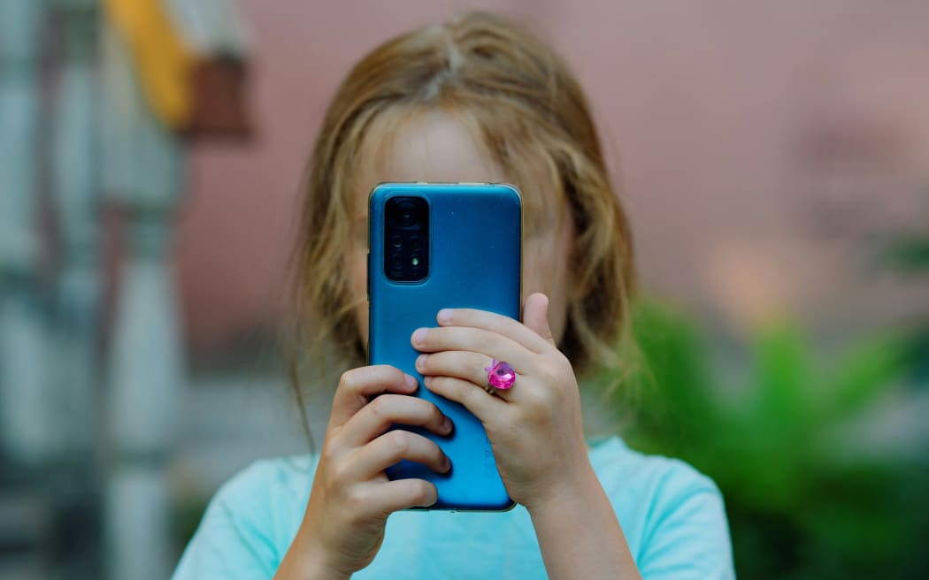 A young girl looks at the screen of a smartphone.