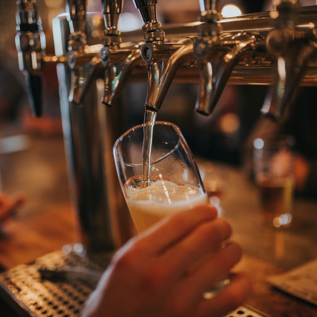 A person's hand can be seen holding a beer glass as the beer pours from a tap in a bar.