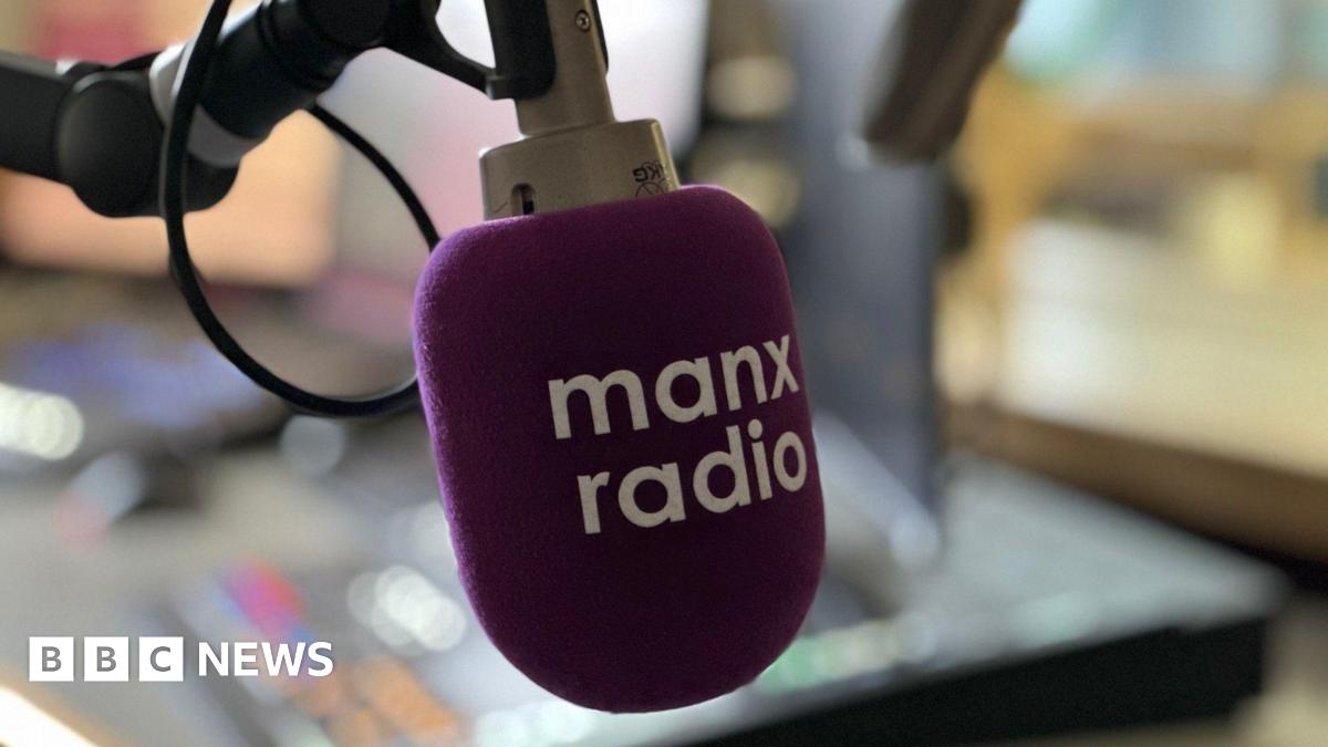 A microphone in a radio studio which has a purple pop shield over it with Manx Radio in white lettering across its face.