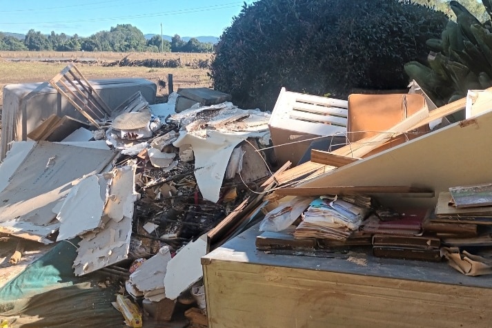 A large pile of rubbish sitting in mud outside a home after a flood.