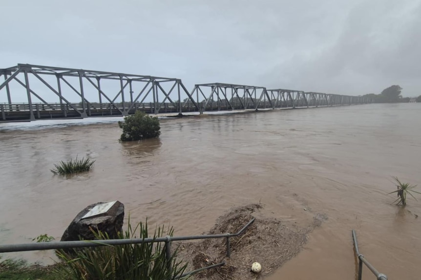 A swollen river with water level just below a long multi-span bridge.